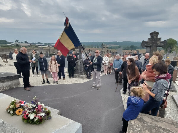 Commémoration du 8 mai 2026 au cimetière de La Croixille. Le maire Serge Deshayes lit le discours officiel devant le monument aux morts fleuri de gerbes. Un porte-drapeau tient le drapeau tricolore. Une trentaine d'habitants, adultes et enfants, assistent à la cérémonie sous un ciel couvert.